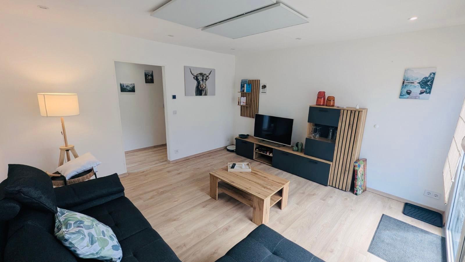 Wohnzimmer einer Ferienwohnung im Allgäu mit Fernseher und elektrischen Rolläden mit Holz-Laminatboden und eine Schlaf-Eckcouch