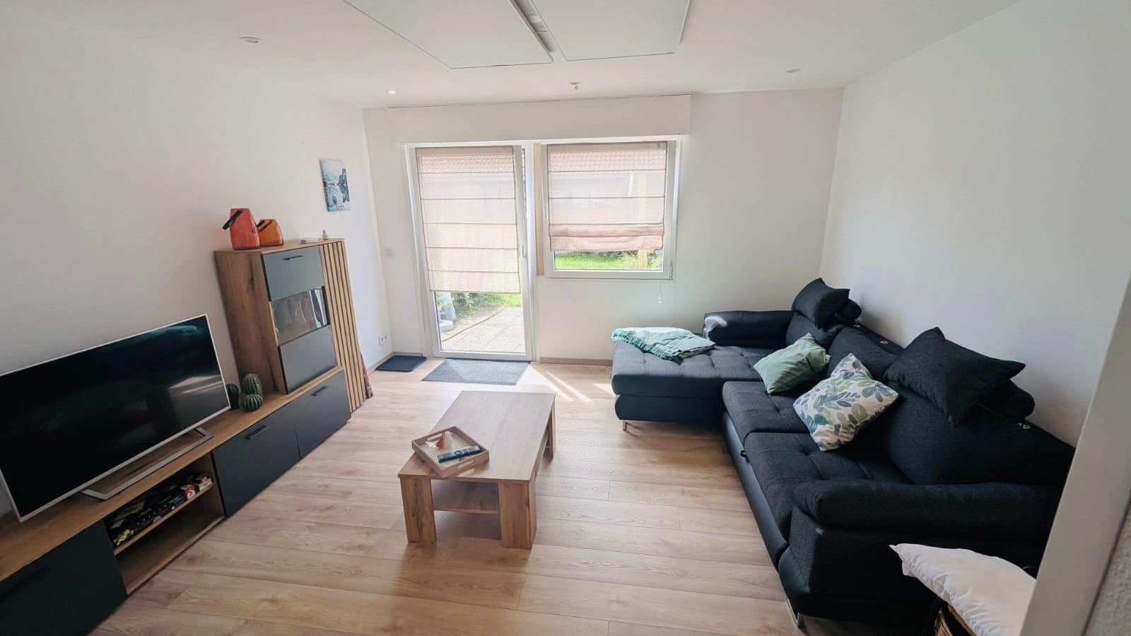 Das Wohnzimmer der Ferienwohnung im Allgäu ist ausgestattet mit einem Holz-Laminatboden, einem Fernseher sowie elektrischen Rollläden. Eine Schlafcouch in Eckform bietet zusätzliche Übernachtungsmöglichkeiten.