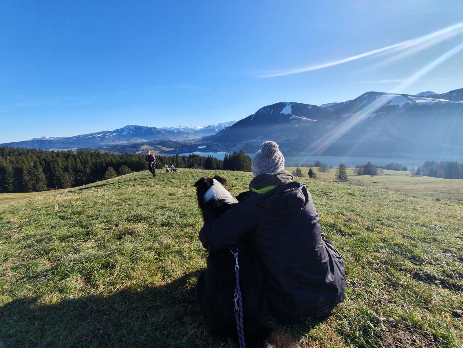 Hund mit Frauchen sitzen auf einer Wiese auf einem Berg und blicken in das Tal